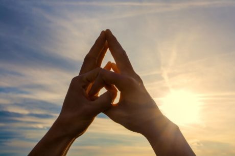 Hands of a hand mudra yoga practitioner with a sunset in the background