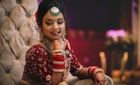 Indian bride in makeup smiling wearing a red wedding gown