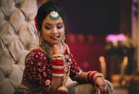 Indian bride in makeup smiling wearing a red wedding gown