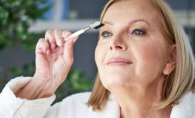 mature woman in white bathrobe putting on makeup