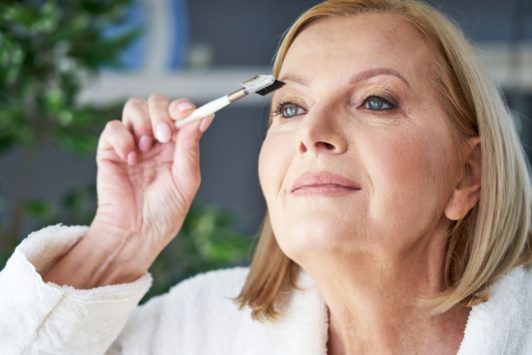 mature woman in white bathrobe putting on makeup
