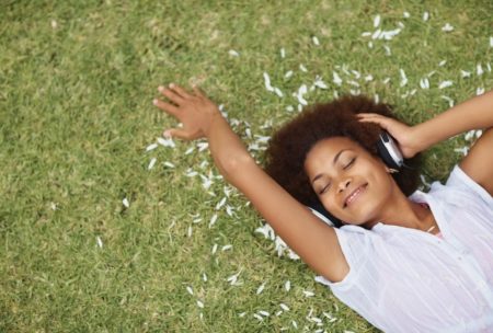 smiling woman in white top laying on grass listening to music on headphone