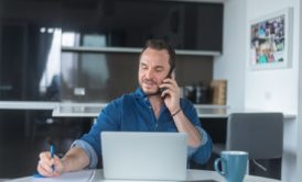 man in blue top talking on phone and writing on paper