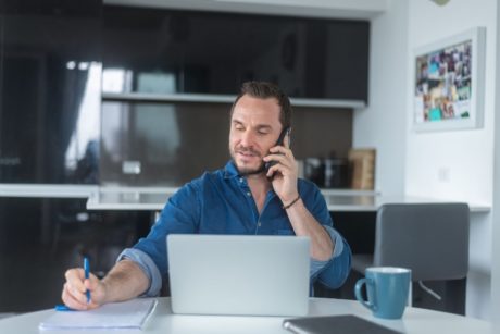 man in blue top talking on phone and writing on paper