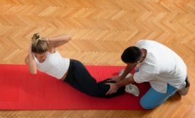 woman doing crunches on red mat with help of male fitness coach