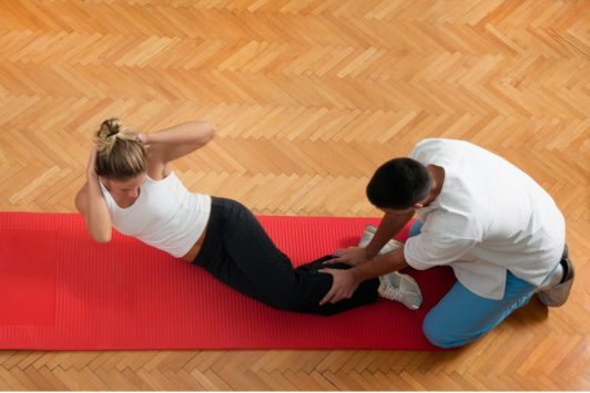 woman doing crunches on red mat with help of male fitness coach