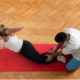 woman doing crunches on red mat with help of male fitness coach