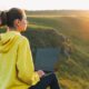 woman in yellow sweatshirt typing on laptop by the hills