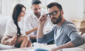 man in grey sweater adjusting glasses with black frame