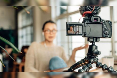 woman wearing light brown sweater recording herself with a camera