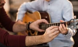 man teaching newbie how to play the guitar