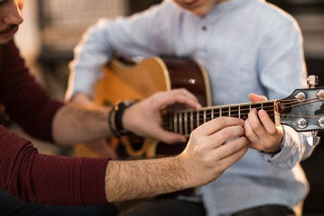 man teaching newbie how to play the guitar