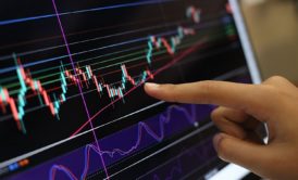 A person pointing at a computer screen showing a stock market chart with volume analysis