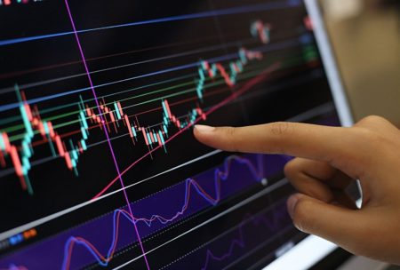 A person pointing at a computer screen showing a stock market chart with volume analysis