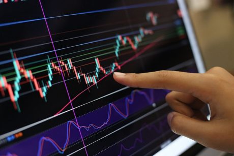 A person pointing at a computer screen showing a stock market chart with volume analysis