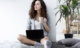 female freelancer holding a cup of coffee and working on laptop