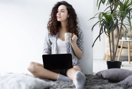 female freelancer holding a cup of coffee and working on laptop