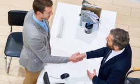 two men at a desk shaking hands, illustrating the culmination of efforts and the essence of closing mastery