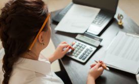 a woman diligently calculates figures on a calculator at her desk, focused on her bookkeeping practice set