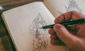 an individual is engaged in basic drawing on a notebook with a pen, illustrating their artistic process and concentration