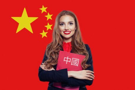 a professional woman in a business suit stands with a folder before the chinese flag, symbolizing business chinese language