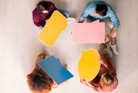 a diverse group of individuals seated on the floor, engaging with colorful speech bubbles during a communication skills training session