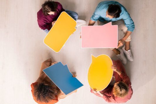 a diverse group of individuals seated on the floor, engaging with colorful speech bubbles during a communication skills training session