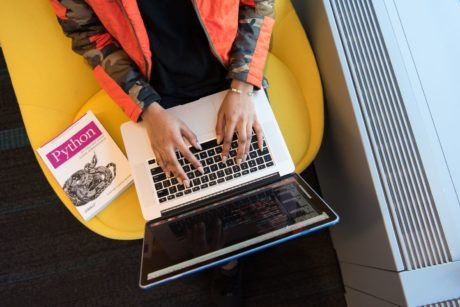 a person sitting on a yellow chair with a laptop, studying the best course in python