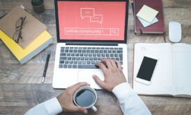 man holding a cup of coffee and typing online community on a laptop