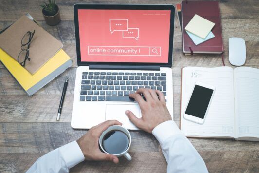 man holding a cup of coffee and typing online community on a laptop