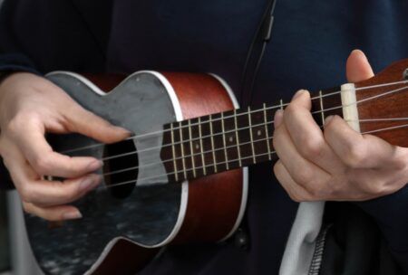 person playing ukulele in park, fingers on basic ukulele chords, surrounded by greenery