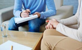 a man and woman engaged in discussion on a couch, using a pen and paper during acceptance and commitment therapy training