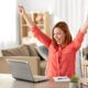 a woman at her desk, arms raised, engaged with her laptop, exemplifying effective time management strategies