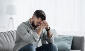 A man on a couch, hands pressed against his face practicing techniques to relieve stress and anxiety