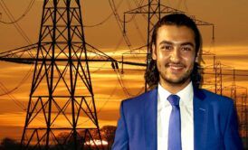 A man in a suit and tie stands before electricity pylons, conducting fault analysis.