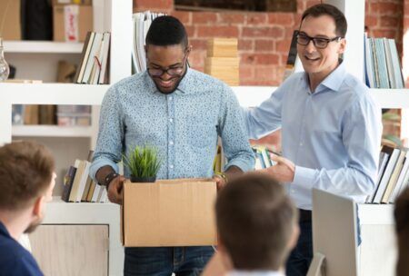 Two men holding a box with a plant, symbolizing the importance of mastering employee onboarding.