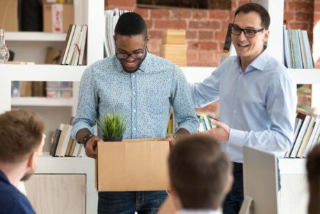 Two men holding a box with a plant, symbolizing the importance of mastering employee onboarding.