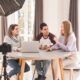 Three people at a table, using a laptop and camera for digital audience engagement.