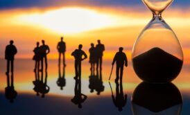 Hourglass symbolizing time with silhouettes of people participating in a Past Life Regression Training session in the background