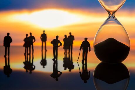 Hourglass symbolizing time with silhouettes of people participating in a Past Life Regression Training session in the background