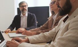 Three people discussing talent management strategies while sitting at a table with a laptop.