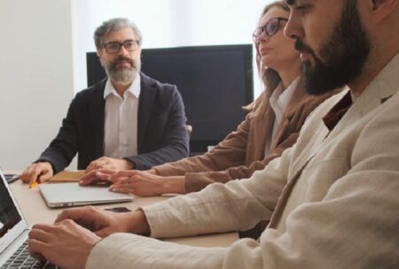 Three people discussing talent management strategies while sitting at a table with a laptop.