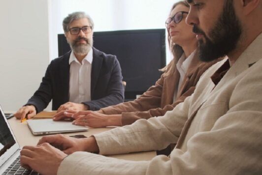 Three people discussing talent management strategies while sitting at a table with a laptop.