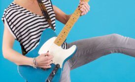 A person in a striped shirt and jeans playing an electric guitar, skillfully mastering guitar chords