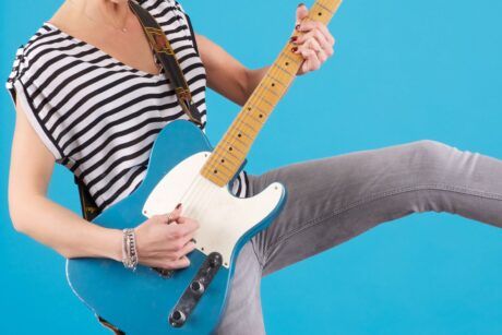 A person in a striped shirt and jeans playing an electric guitar, skillfully mastering guitar chords