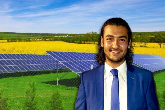 A man in a suit and tie standing in front of solar panels, showcasing solar energy design course