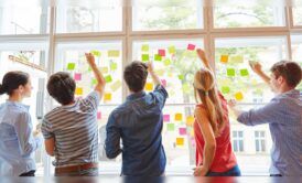 several individuals engaging in team building and problem solving activities by examining sticky notes on a window