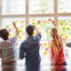 several individuals engaging in team building and problem solving activities by examining sticky notes on a window