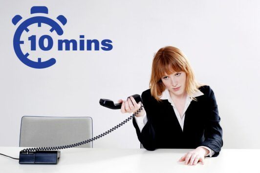 Image of a professional woman at a desk with a phone and a 10 minutes sign, handling abusive customers.