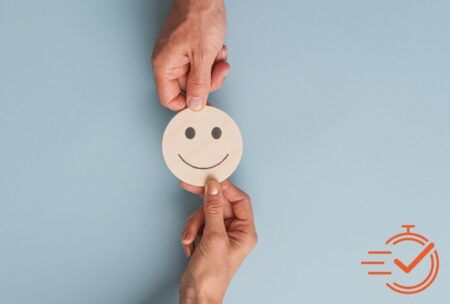 Two hands display a smiley face paper cutout, embodying the joy of coaching and the impact of supportive feedback.